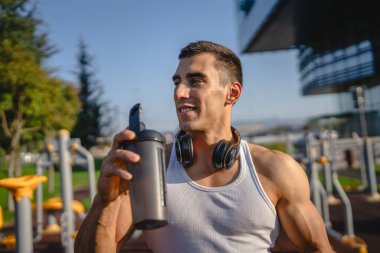 Beyaz tenli genç bir erkek sporcu açık hava spor salonunda çalışırken fren yapıyor. Elinde destek malzemesi tutuyor. Kendine güveni tam, güçlü, güçlü bir kopya alanı var.