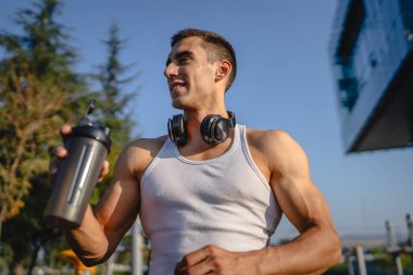 Beyaz tenli genç bir erkek sporcu açık hava spor salonunda çalışırken fren yapıyor. Elinde destek malzemesi tutuyor. Kendine güveni tam, güçlü, güçlü bir kopya alanı var.