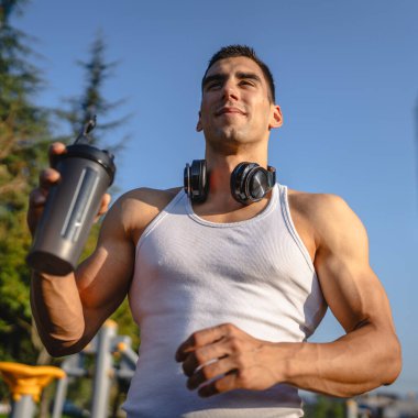 Beyaz tenli genç bir erkek sporcu açık hava spor salonunda çalışırken fren yapıyor. Elinde destek malzemesi tutuyor. Kendine güveni tam, güçlü, güçlü bir kopya alanı var.