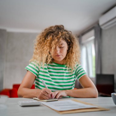 Evdeki beyaz kadın harcamaları ve vergileri hesaplamak için hesap makinesi kullanıyor