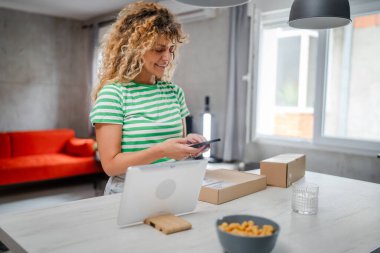 Beyaz bir kadın, online alışveriş ürünlerinin nakliye detaylarını kontrol etmek için akıllı telefon kullanıyor. Akıllı telefon uygulaması başvurusunu kontrol edin. Çevrimiçi detaylar mutlu bir gülümseme.