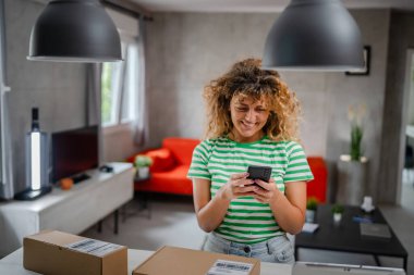 Beyaz bir kadın, online alışveriş ürünlerinin nakliye detaylarını kontrol etmek için akıllı telefon kullanıyor. Akıllı telefon uygulaması başvurusunu kontrol edin. Çevrimiçi detaylar mutlu bir gülümseme.