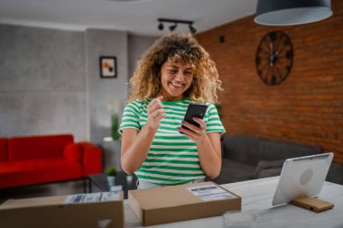 Beyaz bir kadın, online alışveriş ürünlerinin nakliye detaylarını kontrol etmek için akıllı telefon kullanıyor. Akıllı telefon uygulaması başvurusunu kontrol edin. Çevrimiçi detaylar mutlu bir gülümseme.