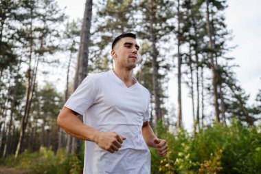 Kafkasyalı genç bir erkek sporcu doğada ormanda koşuyor sonbaharda ya da yazın koşuyor spor yapıyor spor yapıyor sağlıklı yaşam tarzı kavramı gerçek insanlar mekanı kopyalıyor.