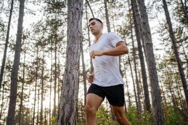 Kafkasyalı genç bir erkek sporcu doğada ormanda koşuyor sonbaharda ya da yazın koşuyor spor yapıyor spor yapıyor sağlıklı yaşam tarzı kavramı gerçek insanlar mekanı kopyalıyor.