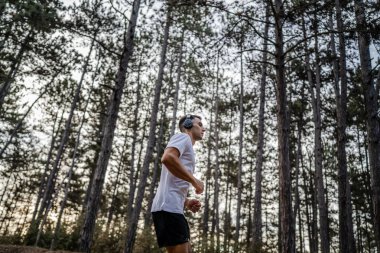 Kafkasyalı genç bir erkek sporcu doğada ormanda koşuyor sonbaharda ya da yazın koşuyor spor yapıyor spor yapıyor sağlıklı yaşam tarzı kavramı gerçek insanlar mekanı kopyalıyor.