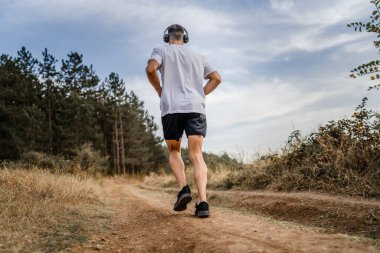 Bir erkek beyaz erkek sporcu doğada toprak yolda koşuyor sonbaharda ya da yazın koşuyor spor yapıyor spor yapıyor sağlıklı yaşam tarzı kavramı gerçek insanlar mekanı kopyalıyor.