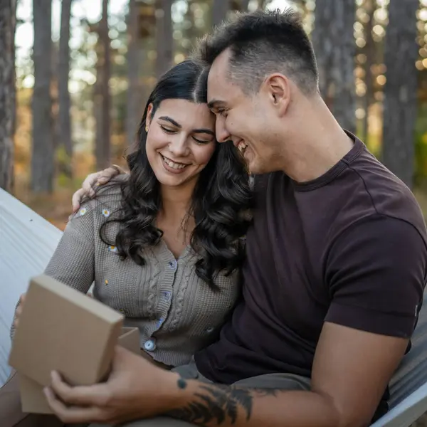 Two people young adult caucasian man and woman couple boyfriend and girlfriend or husband and wife give gift box present while sit in nature forest park celebrate romantic love real people copy space