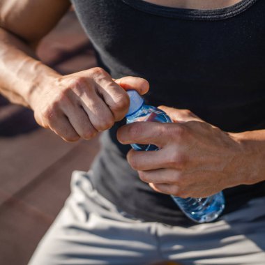 Beyaz tenli bir erkek sporcu plastik su şişesini açık tutuyor ve açık havada güneşli su ve sağlıklı yaşam tarzı konsepti fotokopi çekerken içmeye hazırlanıyor.