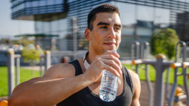 Beyaz tenli bir erkek sporcu plastik su şişesini açık tutuyor ve açık havada güneşli su ve sağlıklı yaşam tarzı konsepti fotokopi çekerken içmeye hazırlanıyor.