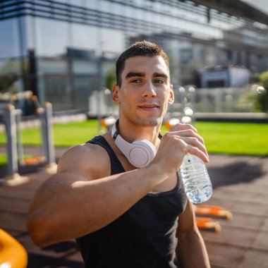 Beyaz tenli bir erkek sporcu plastik su şişesini açık tutuyor ve açık havada güneşli su ve sağlıklı yaşam tarzı konsepti fotokopi çekerken içmeye hazırlanıyor.