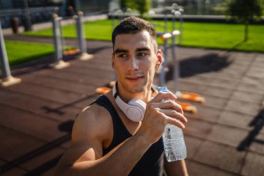 Beyaz tenli bir erkek sporcu plastik su şişesini açık tutuyor ve açık havada güneşli su ve sağlıklı yaşam tarzı konsepti fotokopi çekerken içmeye hazırlanıyor.