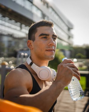 Beyaz tenli bir erkek sporcu plastik su şişesini açık tutuyor ve açık havada güneşli su ve sağlıklı yaşam tarzı konsepti fotokopi çekerken içmeye hazırlanıyor.