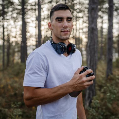 Kafkas kökenli genç bir erkek sporcu açık havada, ormandaki parkta ya da doğadaki ormanlık alanda çalışırken fren yapıyor. Elinde güçlü ve mutlu bir kopya alanı tutuyor.