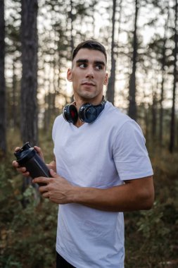 Kafkas kökenli genç bir erkek sporcu açık havada, ormandaki parkta ya da doğadaki ormanlık alanda çalışırken fren yapıyor. Elinde güçlü ve mutlu bir kopya alanı tutuyor.