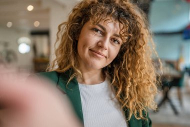 Kafkasyalı mutlu bir kadın kafenin içinde kıvırcık saçlı bir gülümsemeyle duruyor. Gerçek bir insan uzay portresi kopyası UGC Kullanıcı İçeriği