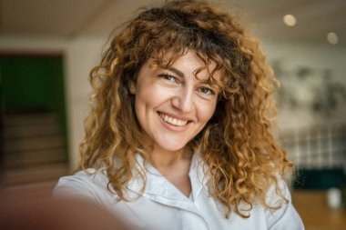 Kafkasyalı mutlu bir kadın kafenin içinde kıvırcık saçlı bir gülümsemeyle duruyor. Gerçek bir insan uzay portresi kopyası UGC Kullanıcı İçeriği
