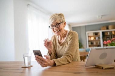 Kafkasyalı yaşlı bir kadın ilaç ya da vitamin takviyesi için evde bir bardak su içen bir kadın internet üzerinden gerçek insanların sağlık hizmetleri konseptini arıyor.