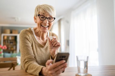 Kafkasyalı yaşlı bir kadın ilaç ya da vitamin takviyesi için evde bir bardak su içen bir kadın internet üzerinden gerçek insanların sağlık hizmetleri konseptini arıyor.
