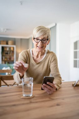 Yaşlı bir beyaz kadın ilaç ya da vitamin takviyesi hapı alıyor. Bir bardak suya koyuyor. Gerçek sağlık hizmetleri konseptinde tedaviyi hazırlıyor.