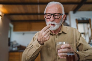 Kafkasyalı bir erkek büyükbaba evde oturur uyuşturucu tableti alır ağrı kesici içer ya da vitamin takviyesi alır. Etikette tıbbın gerçek insan sağlığı ve tıp kavramını okur.
