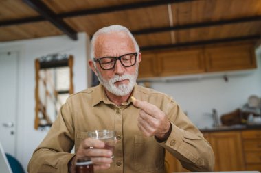 Kafkasyalı bir erkek büyükbaba evde oturur uyuşturucu tableti alır ağrı kesici içer ya da vitamin takviyesi alır. Etikette tıbbın gerçek insan sağlığı ve tıp kavramını okur.