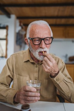 Kafkasyalı bir erkek büyükbaba evde oturur uyuşturucu tableti alır ağrı kesici içer ya da vitamin takviyesi alır. Etikette tıbbın gerçek insan sağlığı ve tıp kavramını okur.