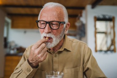Kafkasyalı bir erkek büyükbaba evde oturur uyuşturucu tableti alır ağrı kesici içer ya da vitamin takviyesi alır. Etikette tıbbın gerçek insan sağlığı ve tıp kavramını okur.