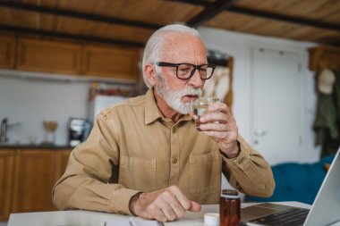 Kafkasyalı bir erkek büyükbaba evde oturur uyuşturucu tableti alır ağrı kesici içer ya da vitamin takviyesi alır. Etikette tıbbın gerçek insan sağlığı ve tıp kavramını okur.