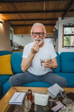 Kafkasyalı bir erkek büyükbaba evde oturur uyuşturucu tableti alır ağrı kesici içer ya da vitamin takviyesi alır. Etikette tıbbın gerçek insan sağlığı ve tıp kavramını okur.