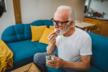 Kafkasyalı bir erkek büyükbaba evde oturur uyuşturucu tableti alır ağrı kesici içer ya da vitamin takviyesi alır. Etikette tıbbın gerçek insan sağlığı ve tıp kavramını okur.