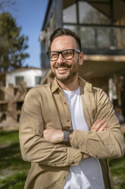 Bir modern yetişkin beyaz erkek portresi sakallı ve gözlüklü erkek evinin önünde duruyor. Mutlu, kendinden emin fotokopi odası.