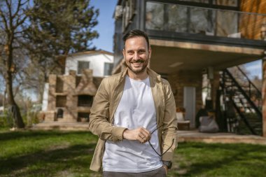 Bir modern yetişkin beyaz erkek portresi sakallı ve gözlüklü erkek evinin önünde duruyor. Mutlu, kendinden emin fotokopi odası.