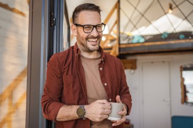 Beyaz erkek, 40 yaşında, balkonda elinde çay ya da kahveyle dikilen bir gömlek giyiyor. Günlük rutininin huzurlu bir anının tadını çıkarıyor. Ya da tatil fotokopi odasında.