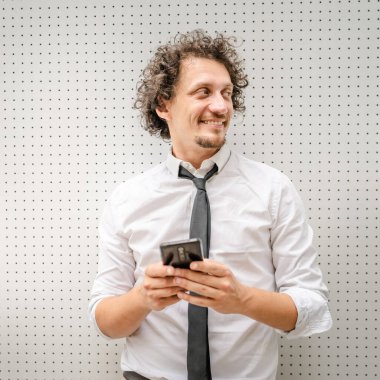 Kafkasyalı bir erkek işadamı telefon etmek ya da mesaj göndermek için akıllı cep telefonu kullanıyor. Açık havada mesaj atıyor. Açık havada beyaz gömlek giyiyor.