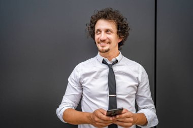 Kafkasyalı bir erkek işadamı telefon etmek ya da mesaj göndermek için akıllı cep telefonu kullanıyor. Açık havada mesaj atıyor. Açık havada beyaz gömlek giyiyor.