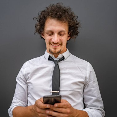 Kafkasyalı bir erkek işadamı telefon etmek ya da mesaj göndermek için akıllı cep telefonu kullanıyor. Açık havada mesaj atıyor. Açık havada beyaz gömlek giyiyor.