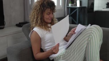 Beyaz bir kadın evde ders çalışıyor. Sınav kağıtlarını okuyup hazırlıyor. Gerçek insanlar kanepede otururken ellerinde kağıt belgeler ya da mektuplar tutuyor. 