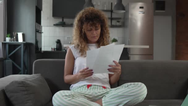 1人の白人女性が自宅で勉強し ソファーベッドに座っている間 実際の人々が紙の文書や郵便物を保持する試験を準備します — ストック動画