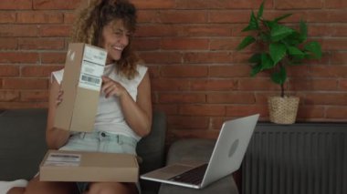 Kafkasyalı yetişkin bir kadın, evde bilgisayarın önünde açık kart okuyup mutlu bir gülücük alıyor. Yavaş çekim çevrimiçi video görüşmesi yapıyor.