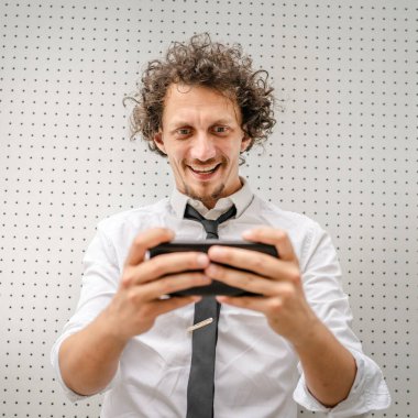 Kafkasyalı bir işadamı dışarıda duruyor mutlu bir gülücük atıyor video oyunları oynuyor, eğleniyor cep telefonu kullanıyor akıllı telefon kullanıyor ve internetteki yetişkin erkeklerin fotokopisini çekiyor.