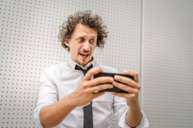 Kafkasyalı bir işadamı dışarıda duruyor mutlu bir gülücük atıyor video oyunları oynuyor, eğleniyor cep telefonu kullanıyor akıllı telefon kullanıyor ve internetteki yetişkin erkeklerin fotokopisini çekiyor.
