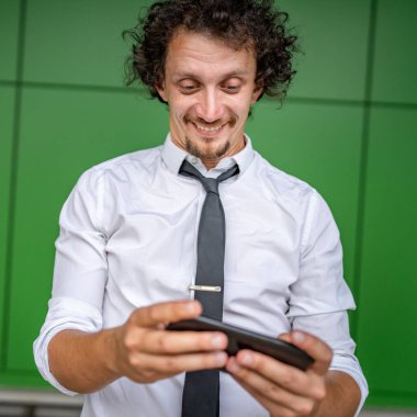 Kafkasyalı bir işadamı dışarıda duruyor mutlu bir gülücük atıyor video oyunları oynuyor, eğleniyor cep telefonu kullanıyor akıllı telefon kullanıyor ve internetteki yetişkin erkeklerin fotokopisini çekiyor.