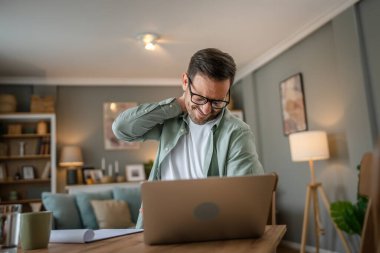 Serbest çalışan bir adam, dizüstü bilgisayarla masa başında çalışırken boyun ağrısı, aşırı çalışma ve yorgunluk konsepti yüzünden sırtı ağrıyordu.