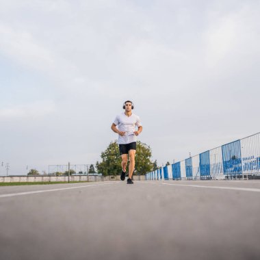 Koşu parkurunda koşan beyaz bir adam. Stadyum erkek sporcusu. Güneşli bahar ve yaz günlerinde koşuyor.