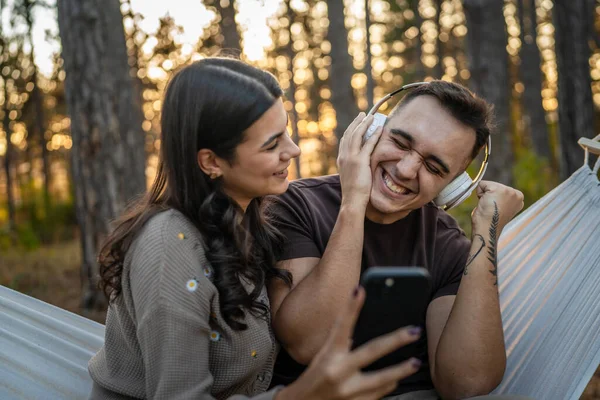 男男女女在自然界中的年轻夫妇听音乐耳机使用手机智能手机或制作视频通话应用程序 — 图库照片
