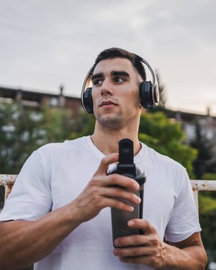 Beyaz tenli genç bir erkek sporcu açık hava eğitimi sırasında fren yapıyor. Elinde destek aleti tutuyor. Kendine güveni tam, güçlü bir kopya alanı.