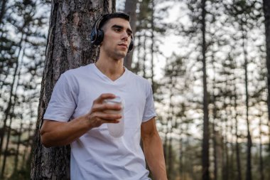 Beyaz tenli genç bir erkek sporcu açık hava eğitimi sırasında fren yapıyor. Elinde destek aleti tutuyor. Kendine güveni tam, güçlü bir kopya alanı.