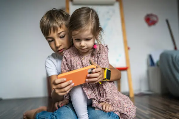 Siblings brother boy hold smartphone with girl sister children use mobile phone smartphone at home in room watch video make a call or play online games leisure family concept real people copy space