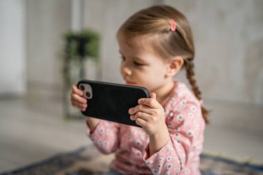 Bir beyaz çocuk cep telefonunu evde tutuyor video oyunları oynuyor ve büyüyen teknoloji bağımlılığı kavramı online tarama veya video izlemek için uygulama kullanıyor